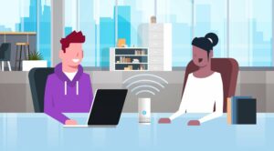 Two people sitting at a desk in an office, using a laptop and a smart speaker between them. Books and an office's interior in the background.